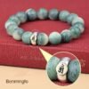 Green bodhi beaded bracelet on red fabric with carved beads and central metal mantra charm