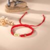 111 angel number bracelet in braided red string with a gold-tone 111 charm plate, on a blush background with dried flowers