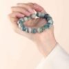 Green bodhi beaded bracelet worn and held in a hand with carved beads and metal charm