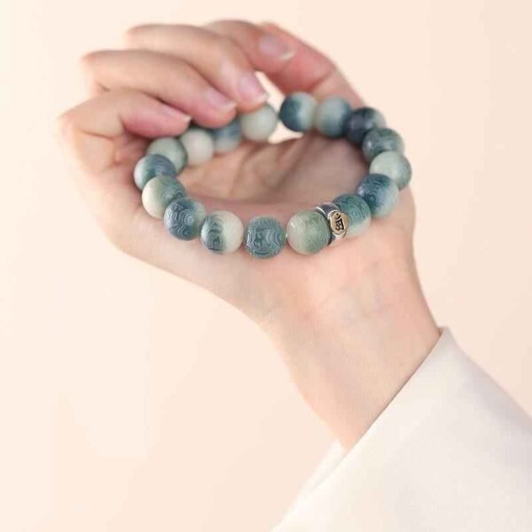 Green bodhi beaded bracelet worn and held in a hand with carved beads and metal charm
