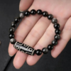 Black obsidian bead bracelet with white-patterned silver tube centerpiece on palm