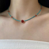 Turquoise bead necklace with round red agate center bead at neckline.