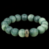 Green bodhi beaded bracelet with carved beads and central metal mantra charm on dark background