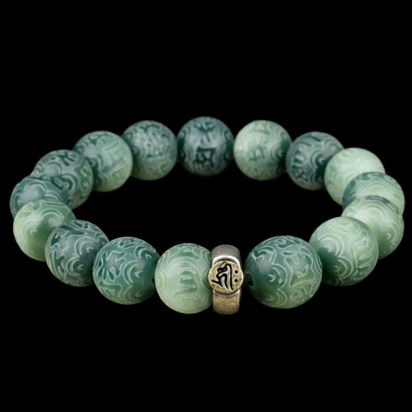 Green bodhi beaded bracelet with carved beads and central metal mantra charm on dark background